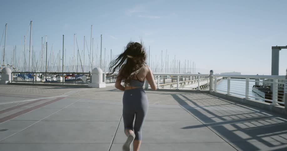 A woman in a sports bra and yoga pants jogs through a marina with sailboats