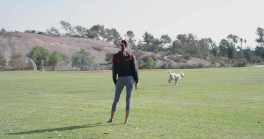 A young woman watches her dog run around a field