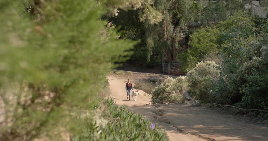 A woman walks her dog along a dirt path