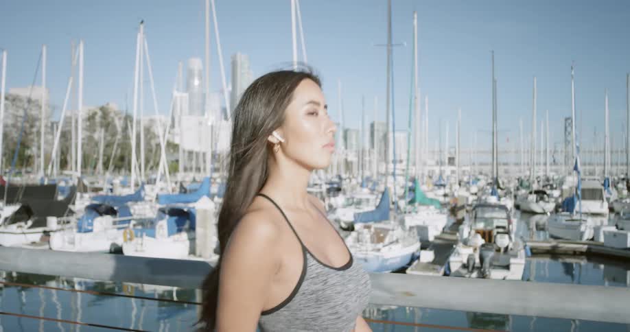 A woman fixes her hair and blocks the sun from her eyes as shes walking by a marina of boats