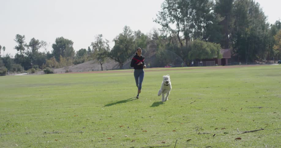 Woman and dog run in the grassy field