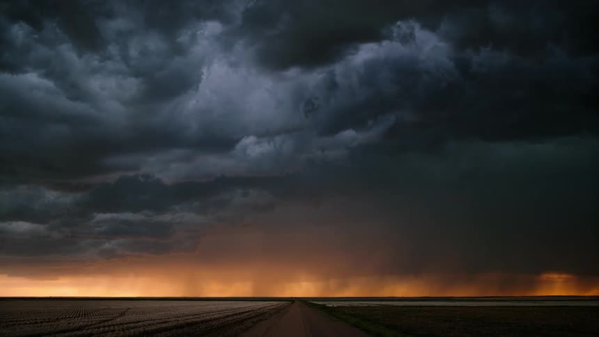 Lightning flashes and rain falls from storm clouds gathered over farm fields and a rural road