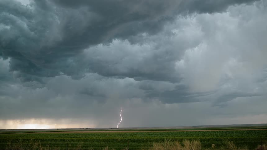A large lightning storm hovers over farm fields