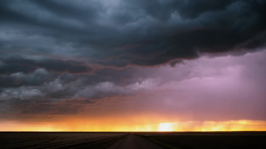 Lightning in heavy clouds over road and fields at sunset