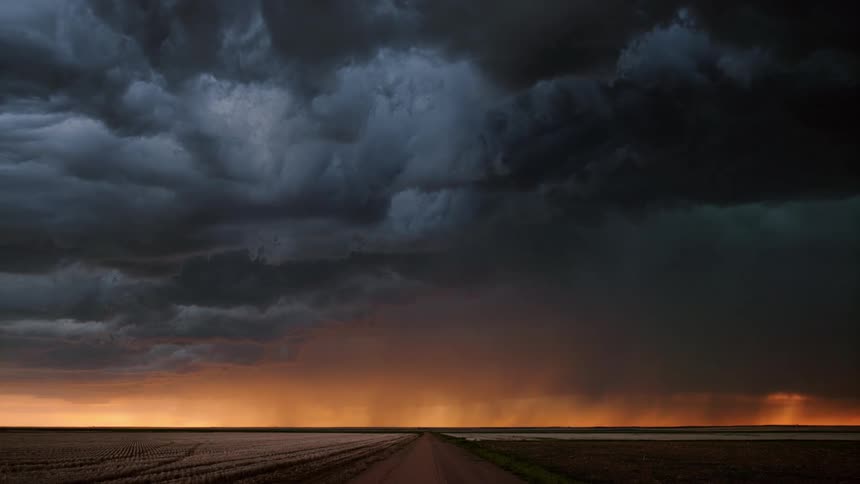 Clouds move over a rural road as lighting flashes from with them