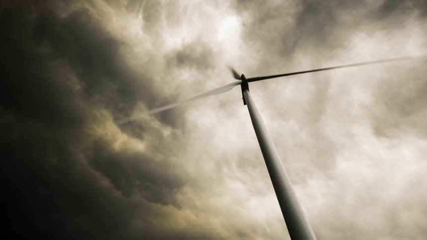 A wind turbine turns in the wind as dark clouds move overhead