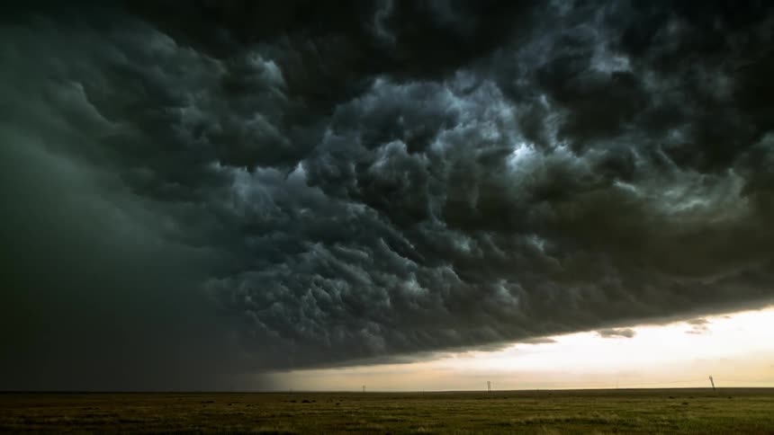 Black storm clouds roll over a grassy plain