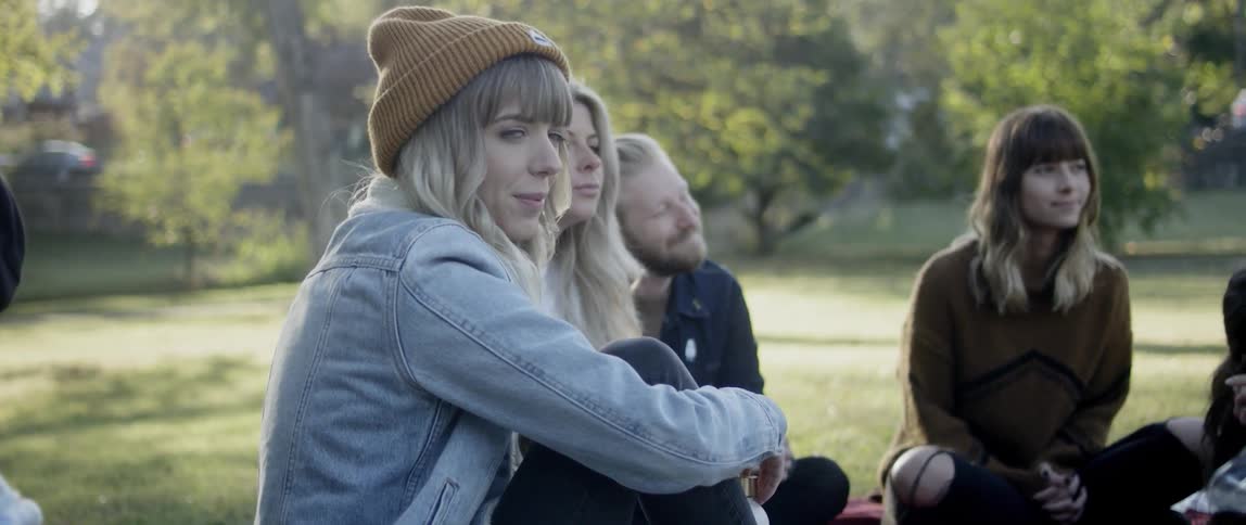 A group of people sitting around on a field in a park