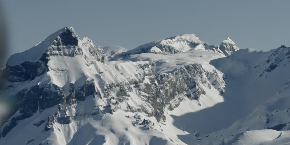 A man in reflective ski goggles walks past snow covered mountains