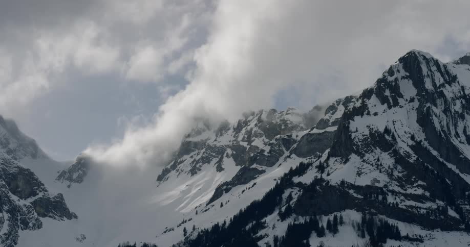 Dense clouds float past a snow covered mountain range