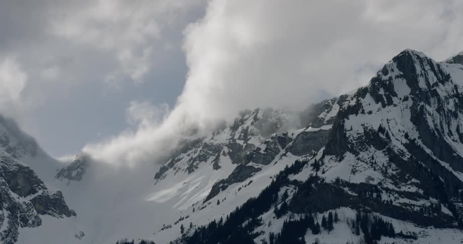 Thick clouds roll by a snowy mountain top
