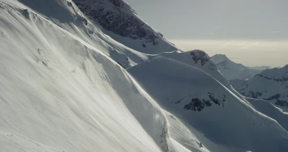 Snow drifts down steep mountain slope