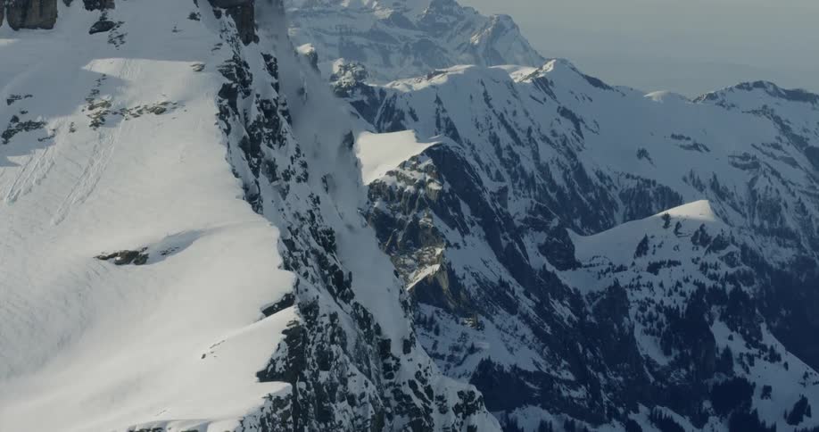 An avalanche falls down rocky mountains during daylight