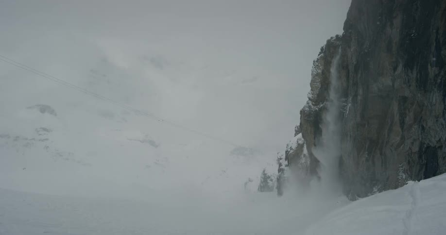 Snow falls down the side of a mountain
