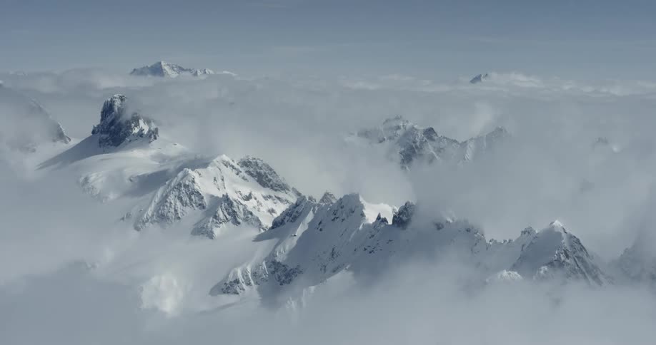 Clouds float at the peaks of snow covered mountains