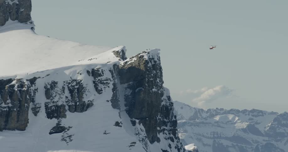 A helicopter hovers beside a snowy mountain