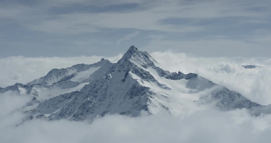 Clouds moving around a snow covered mountain peak during the day