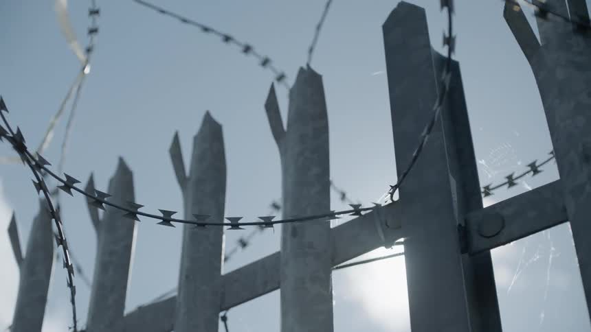 Razor wire tops fence under blue sky
