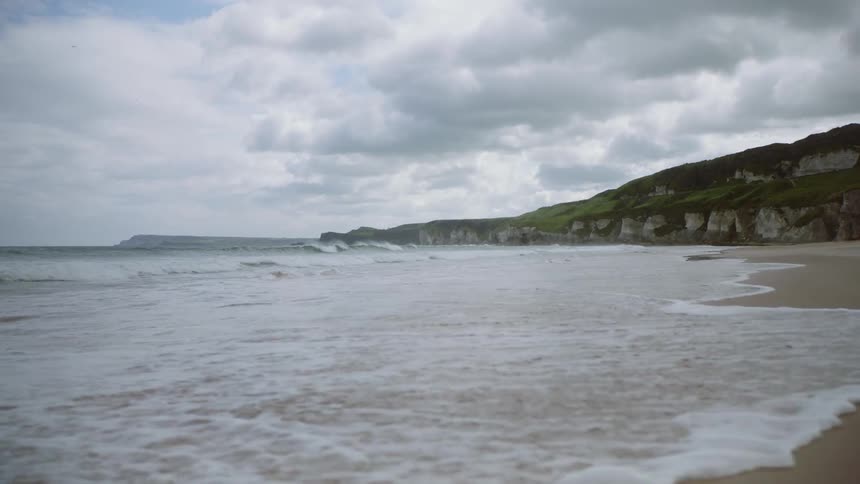 Ocean water flows onto the beach near a cliff