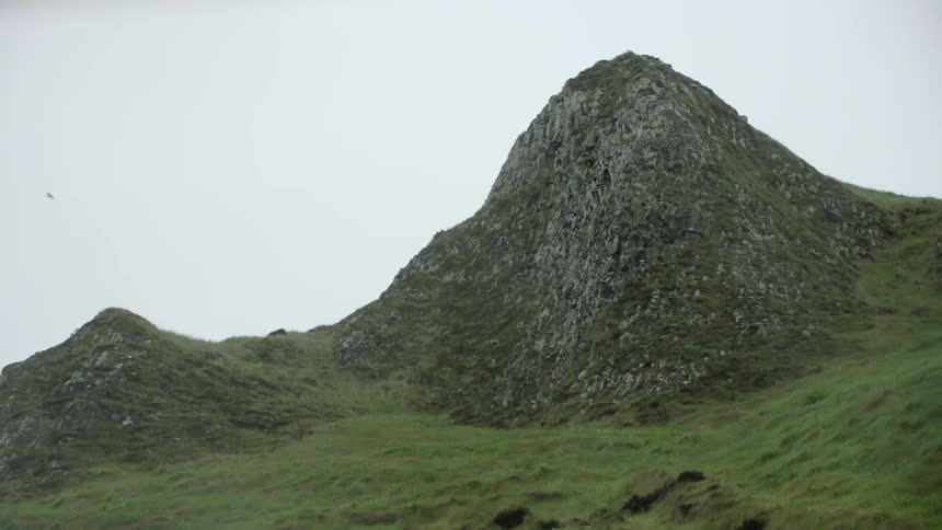 Birds fly around a steep grass covered mountain hill