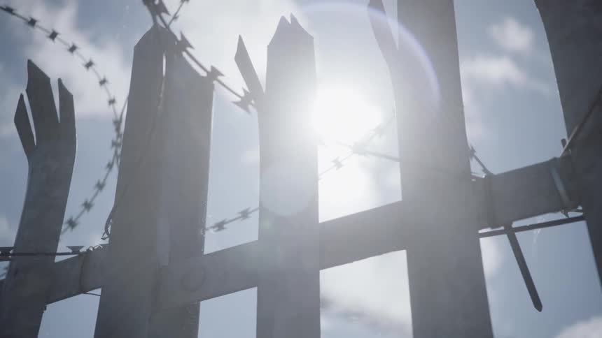 The sun shines down on a fence topped with barbed wire