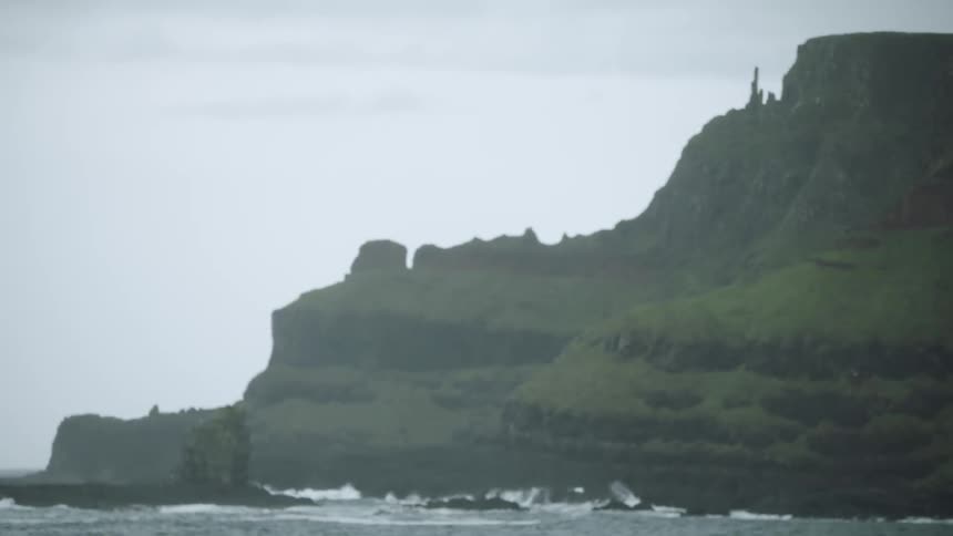 Ocean waves crashing against a tall headland on a cloudy day