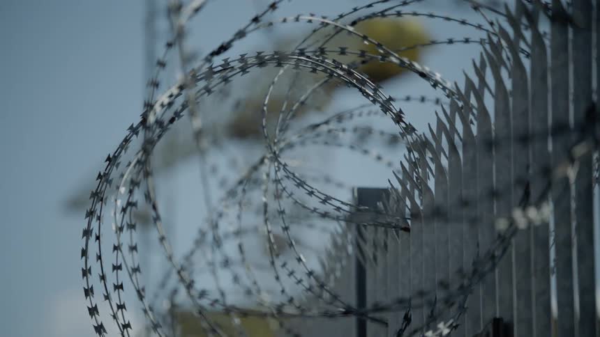 Barbed wire covers a fence leading to a construction crane