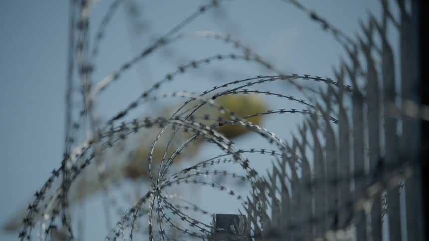 Barbed wire cover a fence leading to a large construction crane
