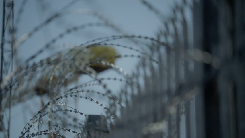 Razor wire on metal fence with crane and tower in background