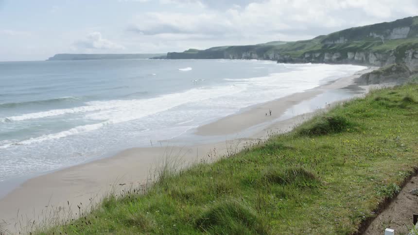 Ocean waves make their way to the sandy shore surrounded by grass and rocks