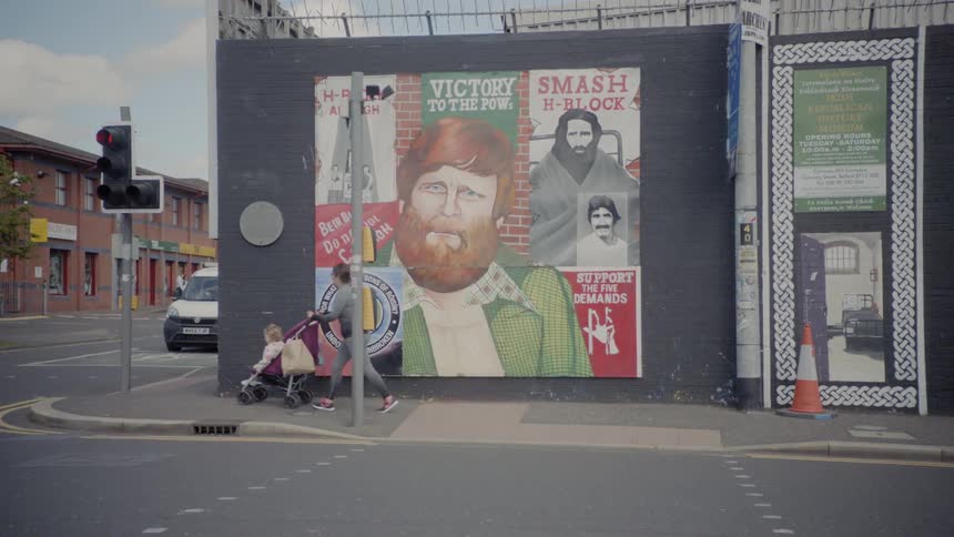 A woman pushing a child in a stroller in front of a street corner with a mural