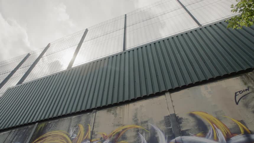 Graffiti tags and paint on a wall topped by a fence