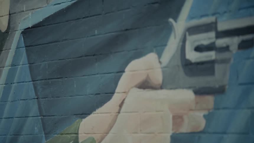 A street painting in ulster shows a male holding a pistol painted on a brick wall