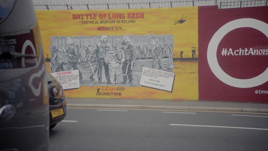 Cars driving past billboards on the side of a wall