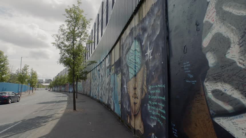 A car travels on a road with a wall covered in murals and graffiti