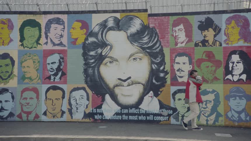 A man walks the sidewalk beside a mural painted on a building