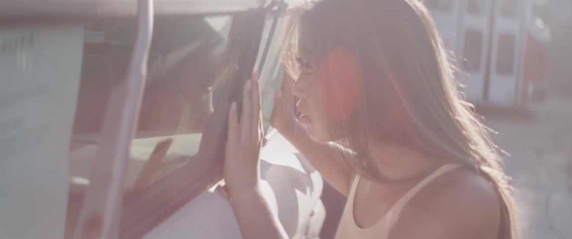 A young adult female places her hands on the window of an older bus while looking inside