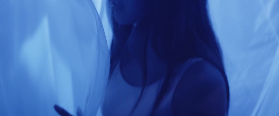 Under the transparent curtains a woman looks around in the blue illuminated room