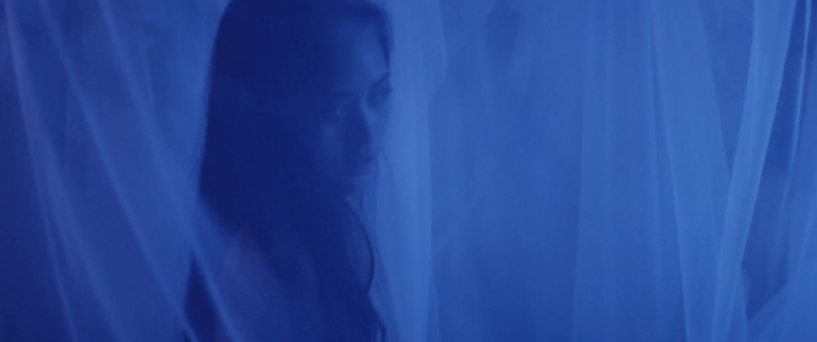 A young woman stands in a tent with veils illuminated by bluish light