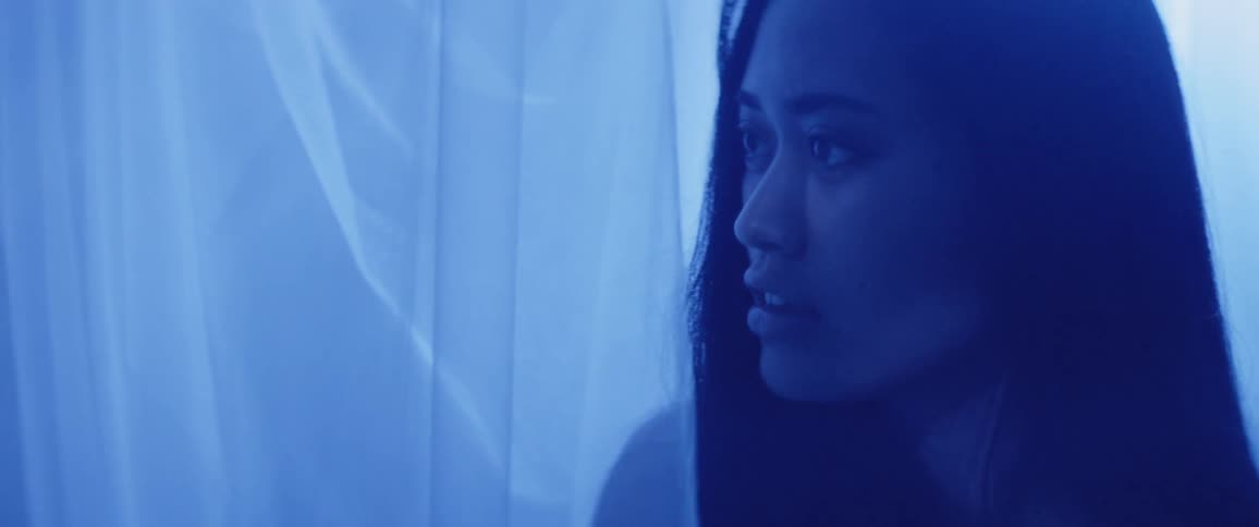 A woman indoors walking towards blue lights and curtains
