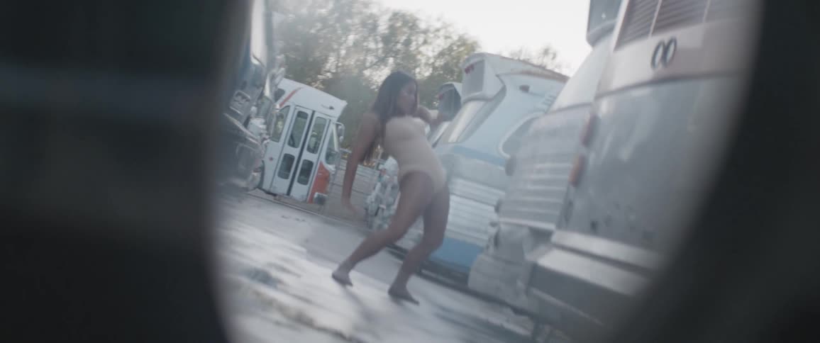 A woman in a bodysuit dances next to retro motorhomes on a sunny day