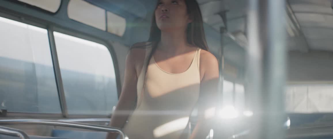 A woman sitting on a bus stare up and stands up while sun shines in through the windows