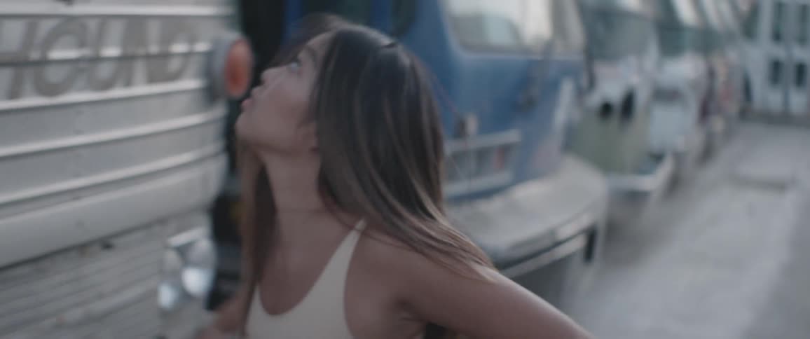 Asian woman dances between two vehicles in the junkyard during daylight