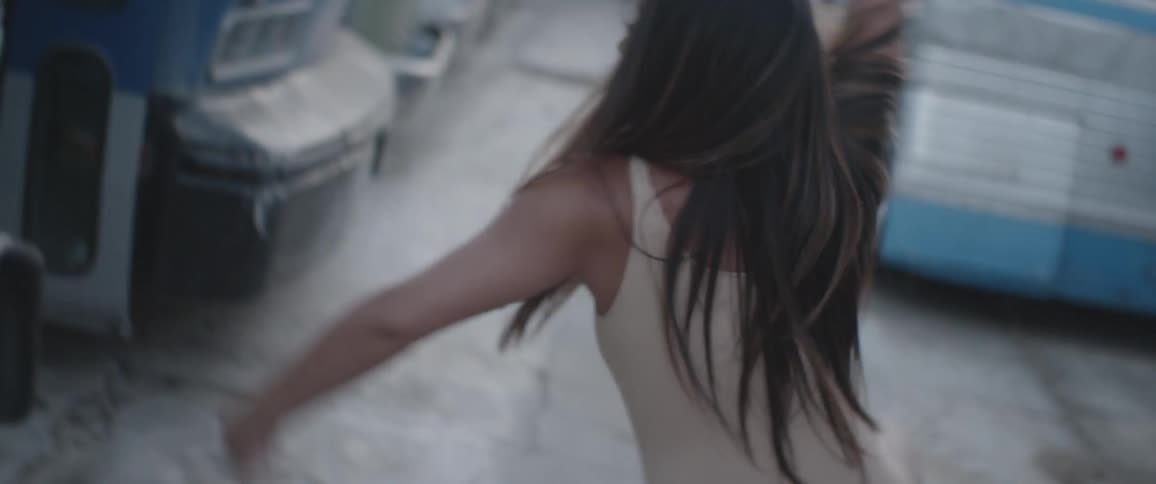 A woman dances in a parking lot full of large oversized vehicles