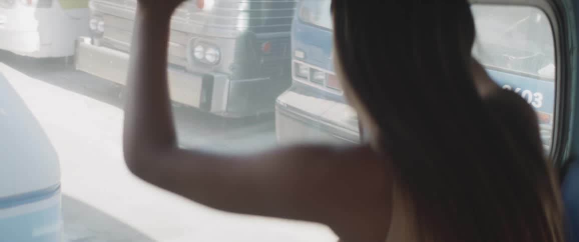 A woman looks out the window of a bus in a bus lot