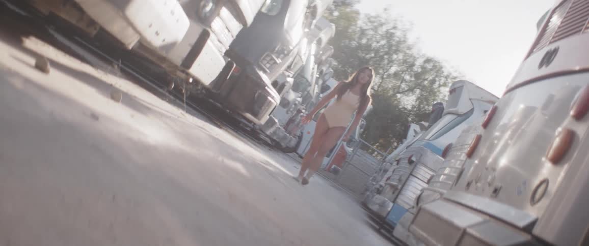 A woman in a bodysuit walks slowly past retro motorhomes on a sunny day