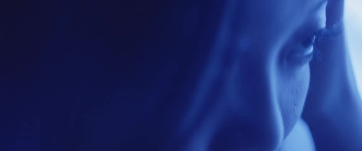 A woman pushes her hair away from her face while looking up from the floor in bluish light