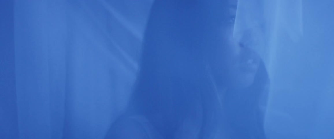 A woman stands in a tent with veils illuminated by electric blue light
