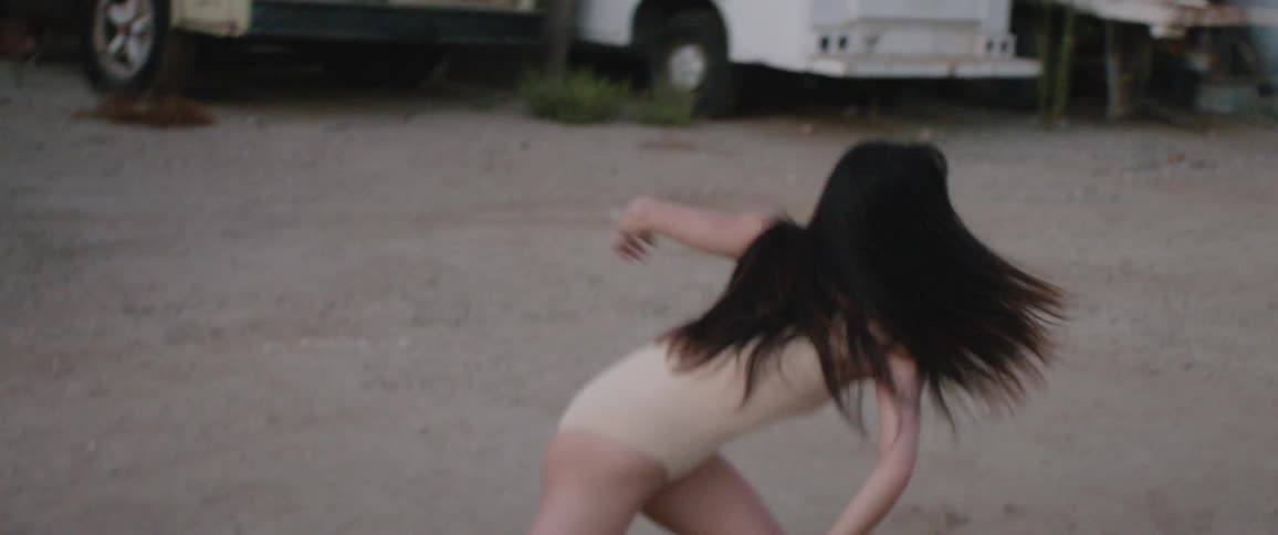 Asian woman dances on the dirt road in the junkyard during daylight
