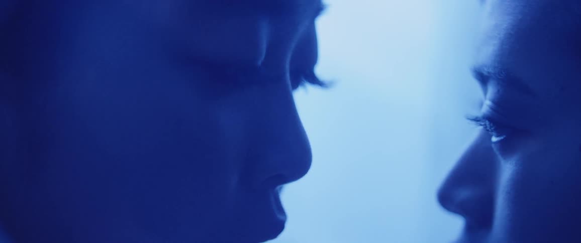 Two women look at each one another in the eyes in a tent illuminated by a bluish light
